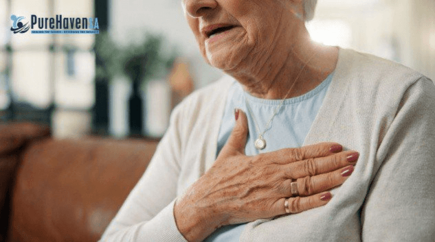 A close-up shot of an elderly woman holding her hand over her chest in discomfort, featuring a "PureHaven SA" logo overlay in the top left corner.